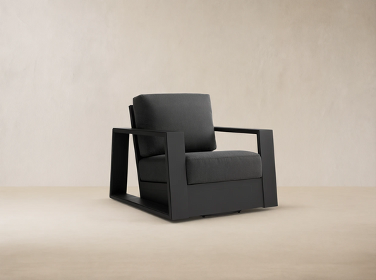 Canyon Outdoor Aluminum Swivel Chair, angled right. Dark charcoal powder-coated frame with thick gray cushions on a stone patio.