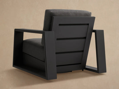 Side view of a modern Canyon Outdoor Swivel Chair. Dark gray aluminum frame and matching cushions against a beige wall.