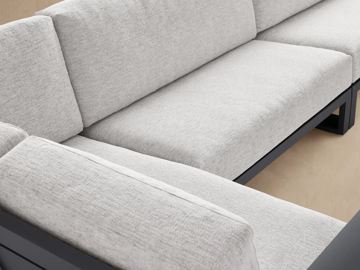 L-shaped Canyon Outdoor Aluminum Sectional with dark gray angular frame, light gray cushions, on a light stone patio.
