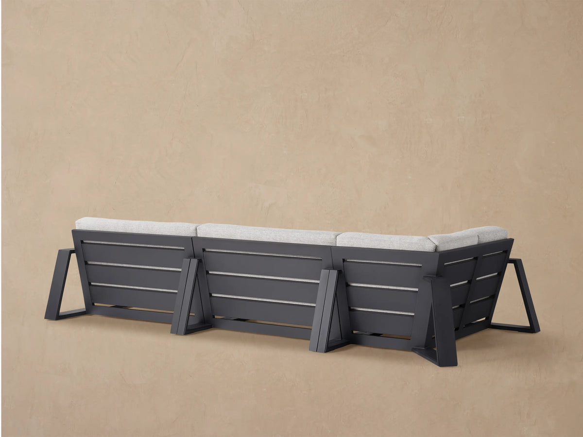 Close-up angled view of a Canyon Outdoor Aluminum Three-Piece Sectional with light gray textured cushions and a dark frame.
