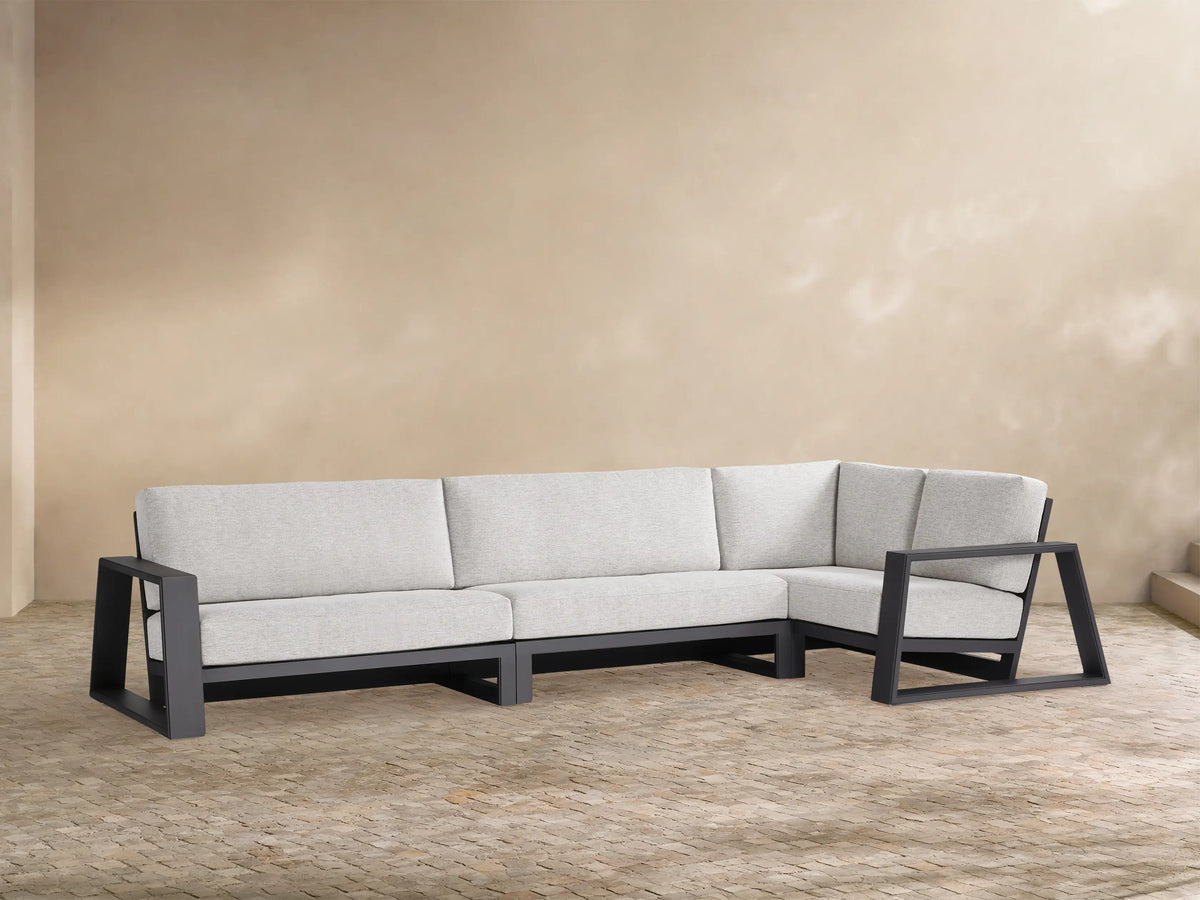 Canyon Outdoor Aluminum Three-Piece Sectional, L-shaped. Dark grey frame, light grey cushions. Modern design on a tan patio.
