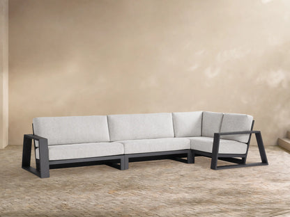 Canyon Outdoor Aluminum Three-Piece Sectional, L-shaped. Dark grey frame, light grey cushions. Modern design on a tan patio.