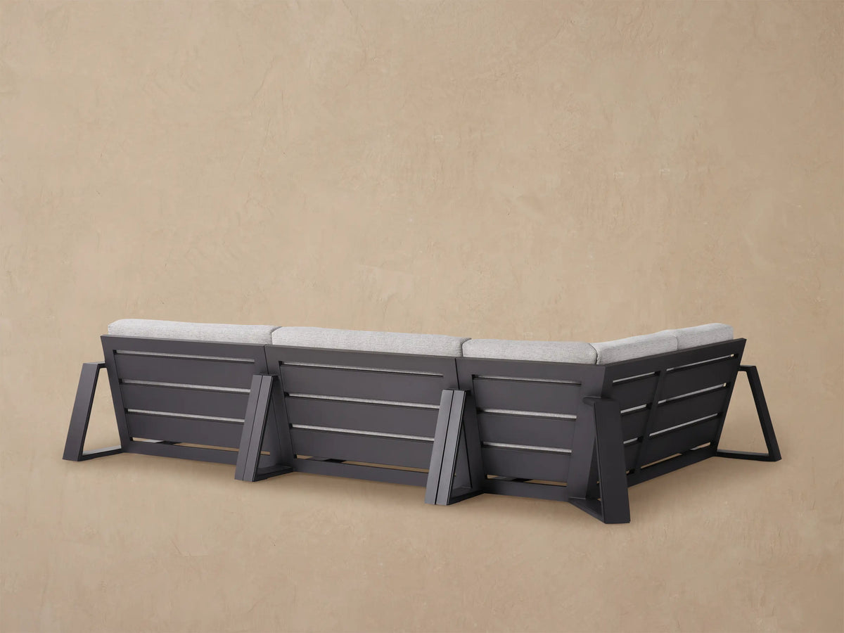 Close-up of Canyon Outdoor Aluminum Sectional corner with light gray textured cushions & dark frame against a tan background.