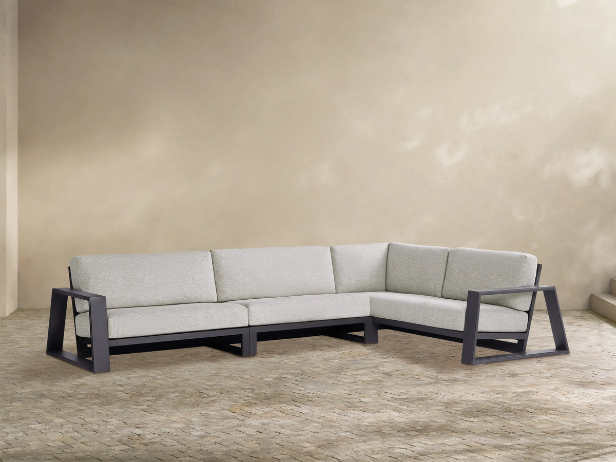 Canyon Outdoor L-shaped three-piece sectional with dark gray aluminum frame & light gray cushions on a tan paver patio.