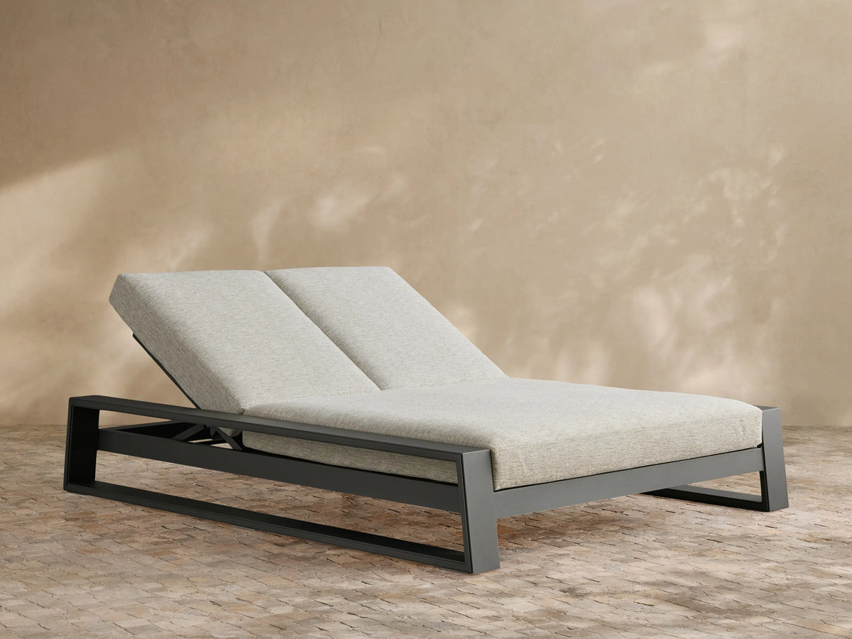 Canyon Outdoor Aluminum Double Chaise with angled backrests, dark gray frame, and light gray cushions on a patio.