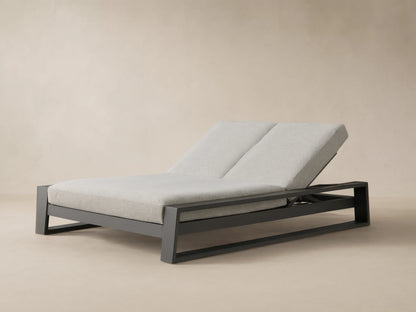 Canyon Outdoor Aluminum Double Chaise with angled backrests, dark gray frame, and light gray cushions on a patio.