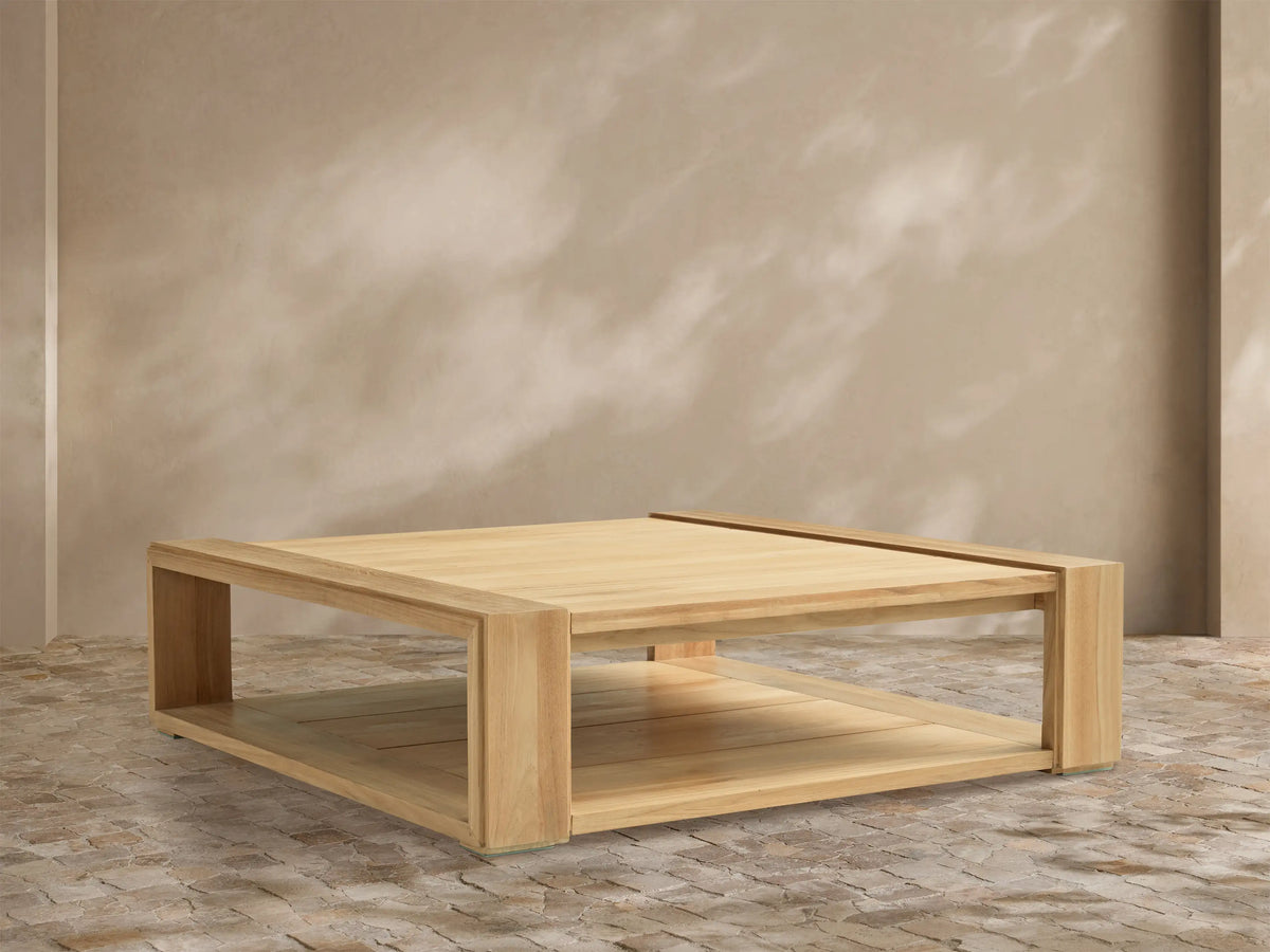 Canyon Outdoor Teak Coffee Table, rectangular, natural light wood, thick block legs, slatted lower shelf, on stone patio.