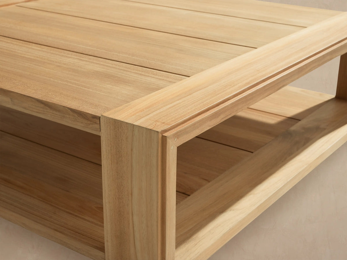 Square Canyon Outdoor Teak Coffee Table, angled view, natural light wood, with a lower slatted shelf, on a stone patio.