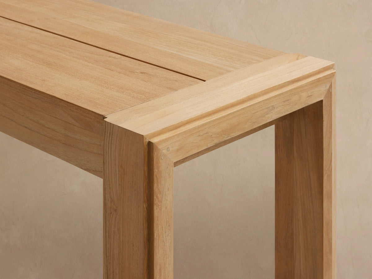 Light natural wood Canyon Outdoor Teak Dining Bench with sturdy rectangular legs, shown at a slight angle against a light background.