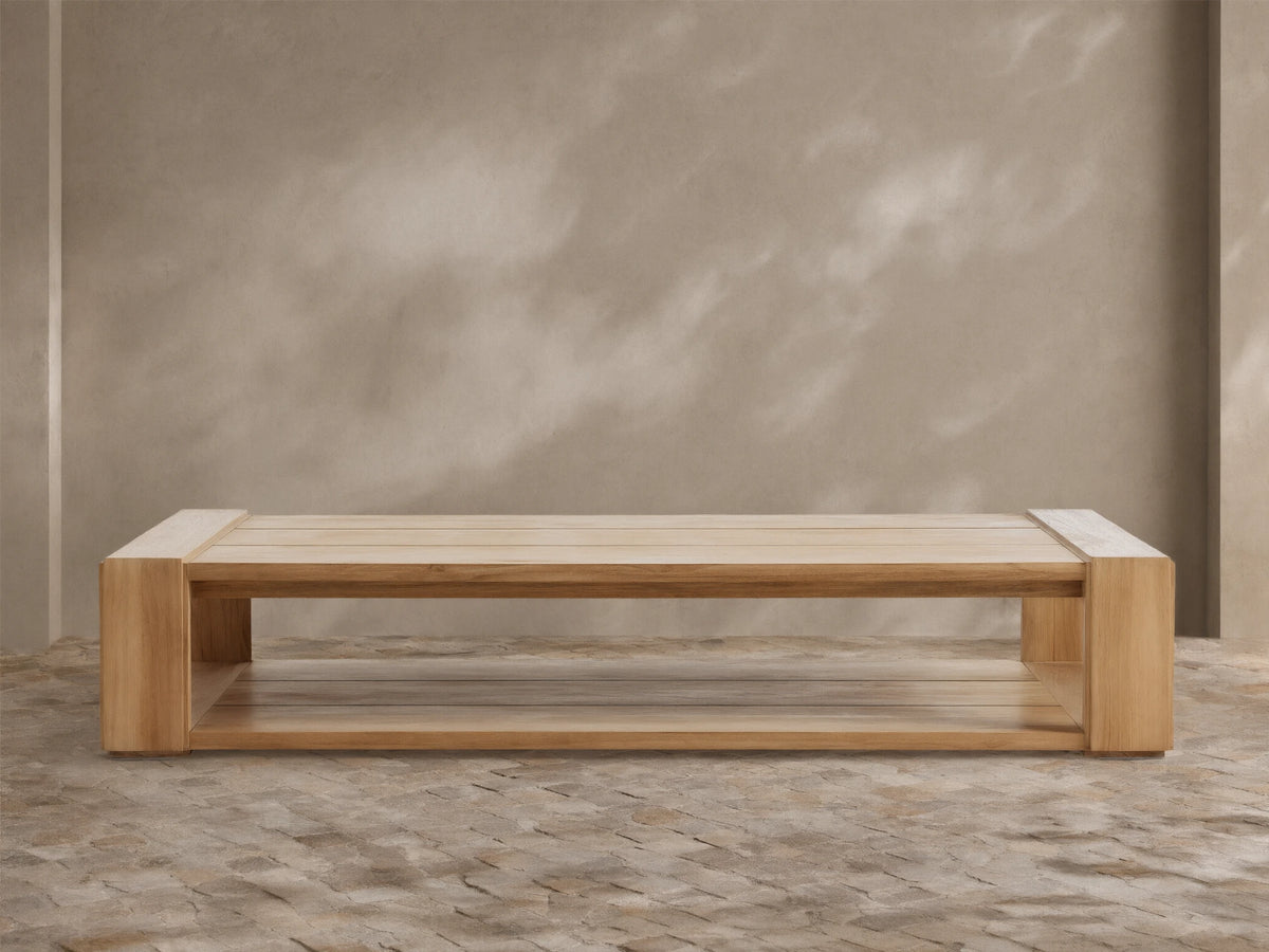 Canyon Outdoor Teak Coffee Table: a rectangular light natural wood table with slatted top & lower shelf, on a stone patio.