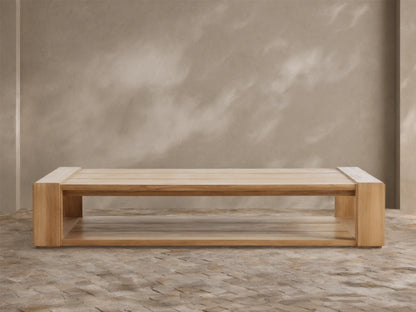 Canyon Outdoor Teak Coffee Table: a rectangular light natural wood table with slatted top & lower shelf, on a stone patio.