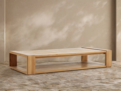 Canyon Outdoor Teak Coffee Table: a rectangular light natural wood table with slatted top & lower shelf, on a stone patio.