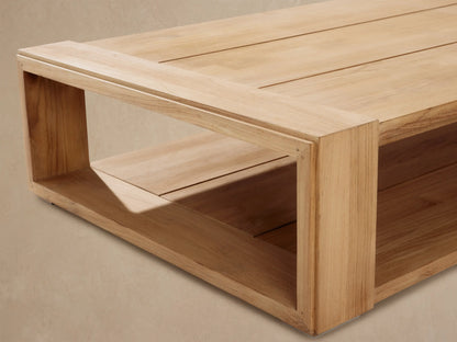 Canyon Outdoor Teak Coffee Table, rectangular light natural teak wood with slatted top and lower shelf on rustic patio.