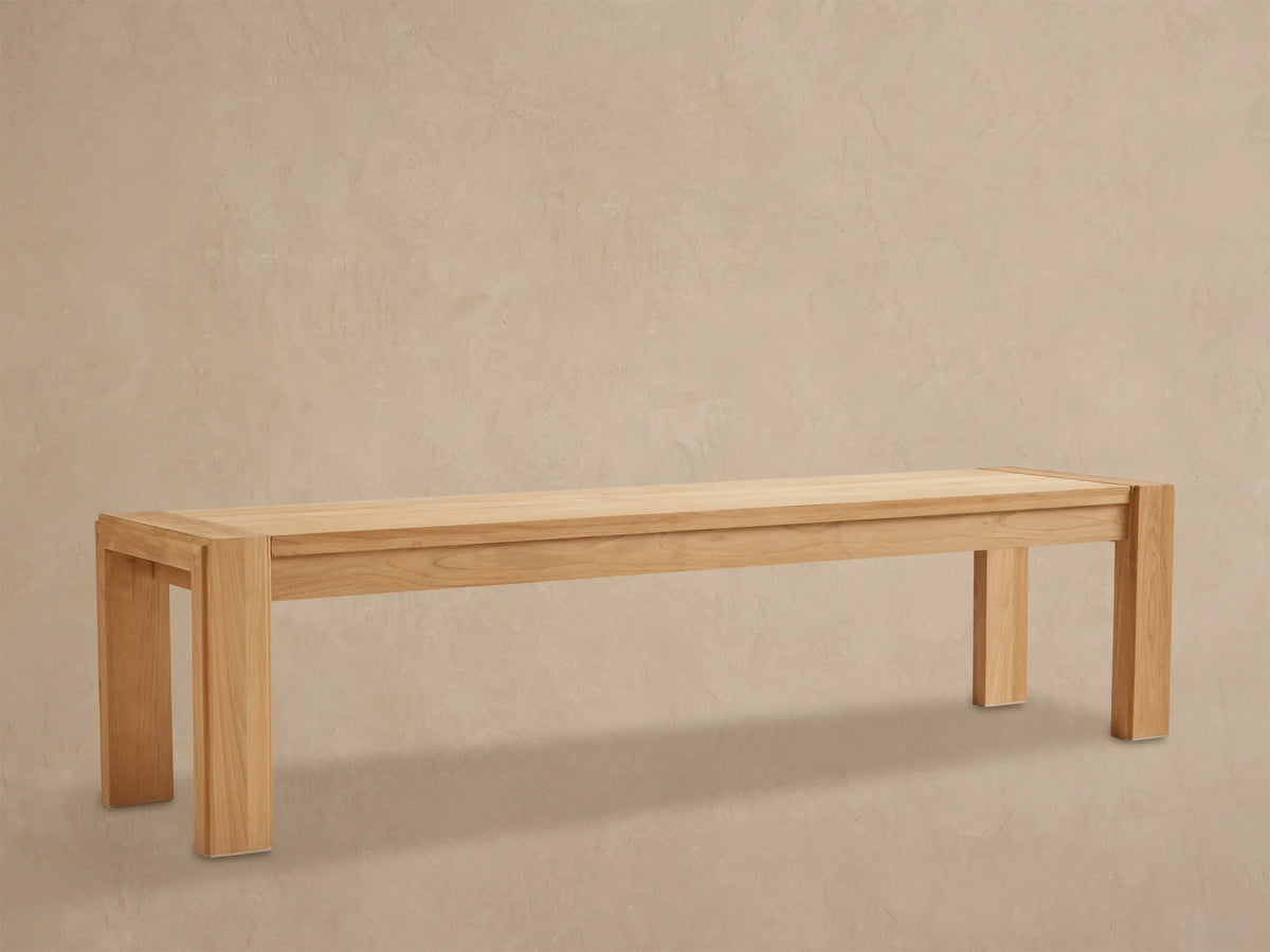 Long, light natural teak wood Canyon Outdoor Dining Bench with sturdy block legs on a stone patio.