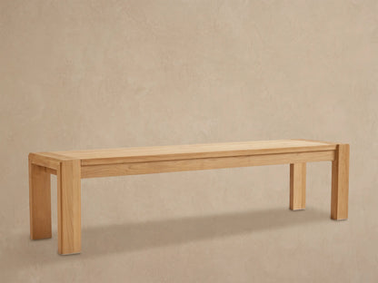 Long, light natural teak wood Canyon Outdoor Dining Bench with sturdy block legs on a stone patio.
