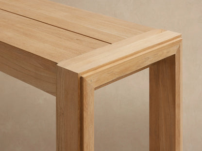 Light blonde teak wood Canyon Outdoor Dining Bench, rectangular seat, thick square legs, angled view on neutral background.