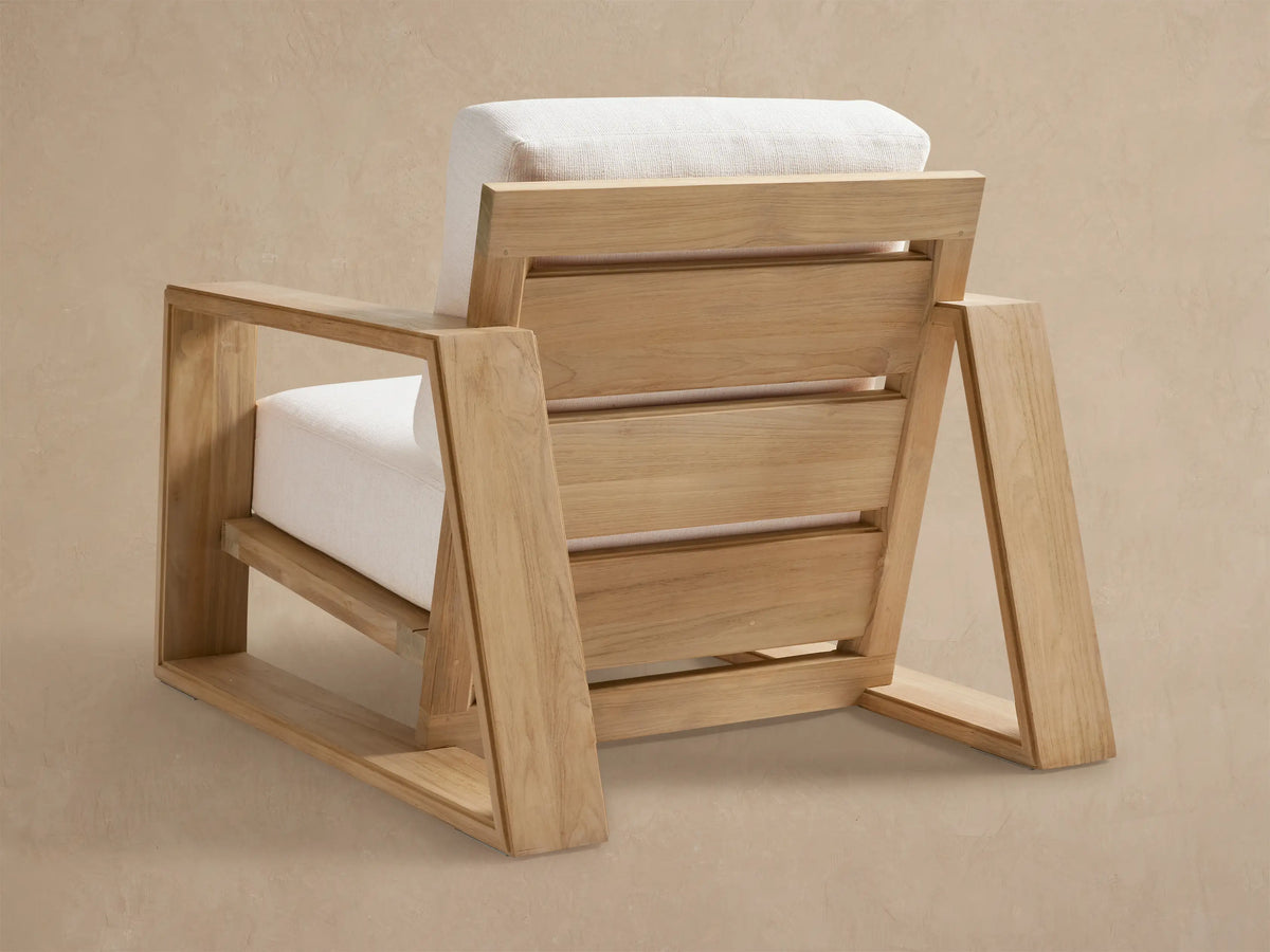 Angled view of Canyon Outdoor Teak Lounge Chair, showing its natural teak wood frame and light-colored, textured cushions.