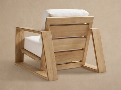 Angled view of Canyon Outdoor Teak Lounge Chair, showing its natural teak wood frame and light-colored, textured cushions.