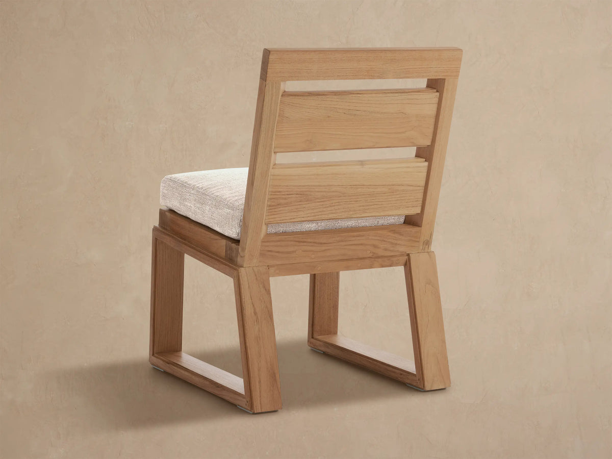 Angled close-up of Canyon Teak Dining Side Chair. Natural teak wood frame with light beige fabric cushion.
