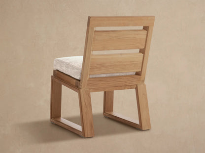 Angled close-up of Canyon Teak Dining Side Chair. Natural teak wood frame with light beige fabric cushion.