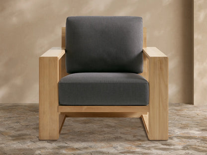 Canyon Outdoor Teak Lounge Chair with geometric natural teak wood frame and dark gray cushions on a stone patio.
