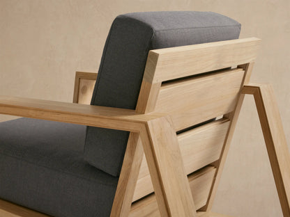 Canyon Outdoor Teak Lounge Chair, front view. Light natural teak frame with thick dark gray cushions on a tiled patio.