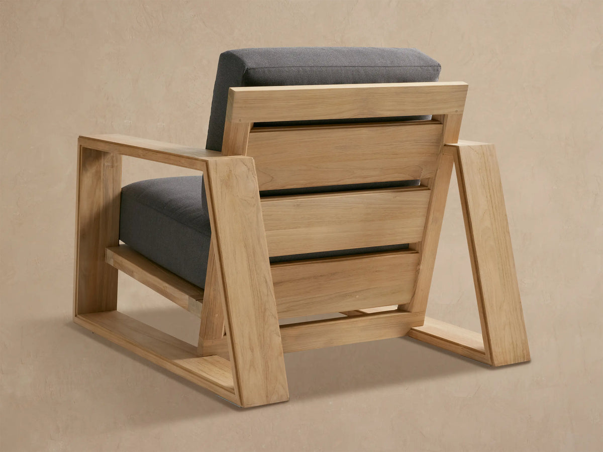 Canyon Outdoor Teak Lounge Chair, natural teak wood frame, dark gray cushions. Angled close-up of slatted back and armrest.