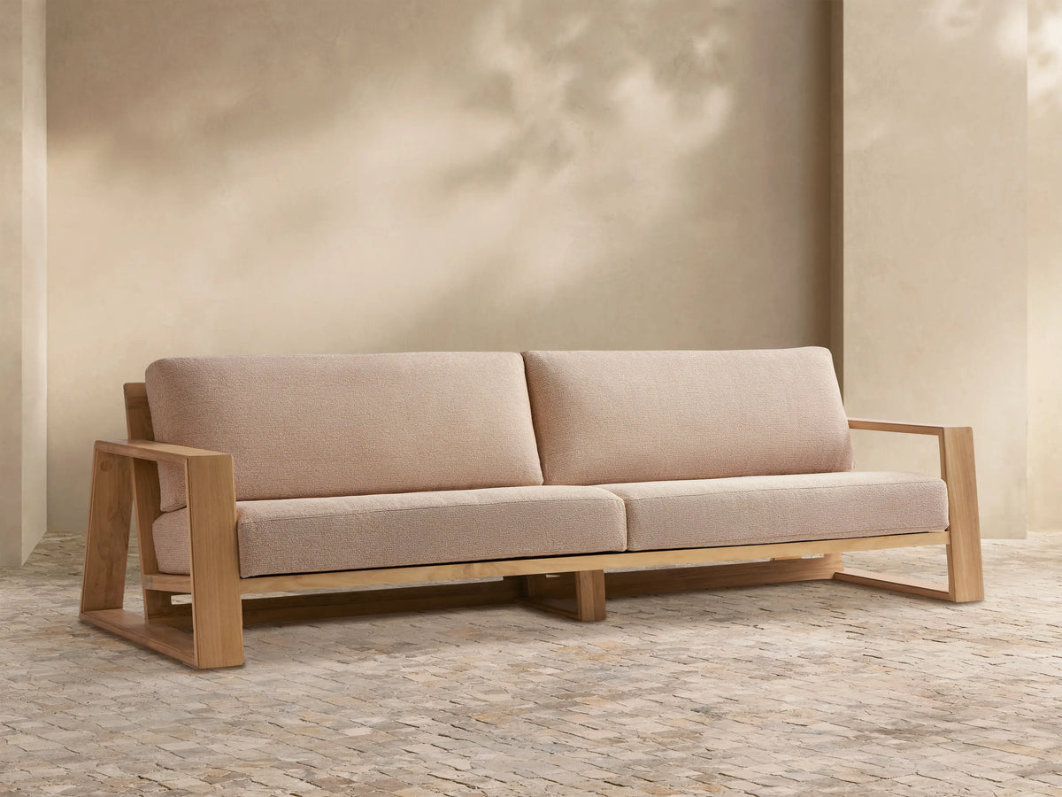Canyon Outdoor Teak Sofa with light teak wood frame and light beige cushions, shown frontally in an outdoor setting.