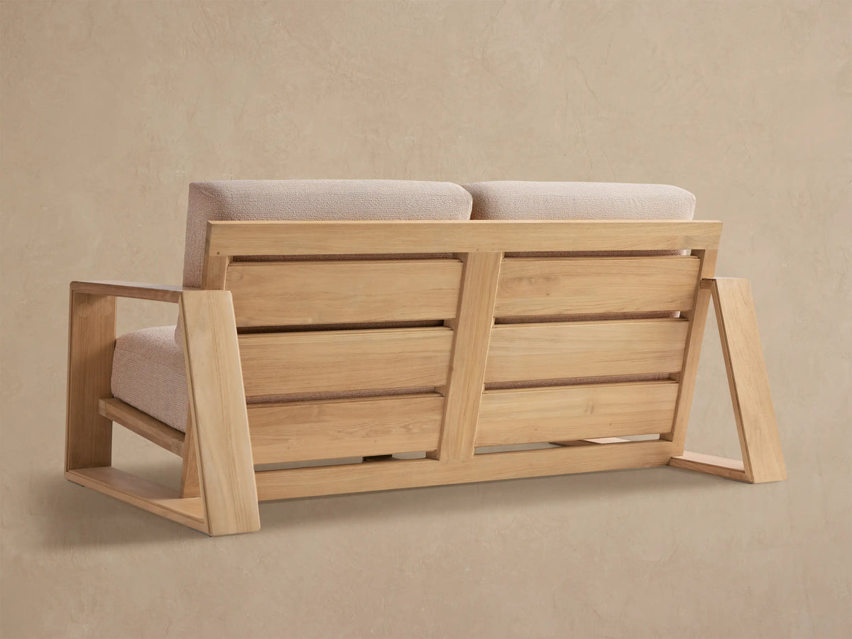 Close-up of Canyon Outdoor Teak Sofa. Light natural teak wood frame with textured beige cushions, angled view.