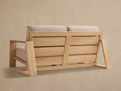 Close-up of Canyon Outdoor Teak Sofa. Light natural teak wood frame with textured beige cushions, angled view.