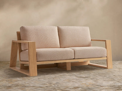 Canyon Outdoor Teak Sofa with natural light teak frame & four light beige textured cushions on a stone floor.