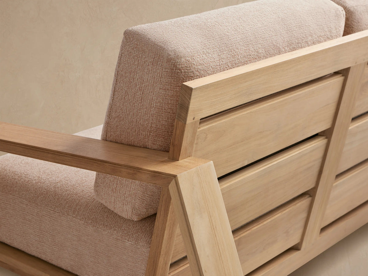 Canyon Outdoor Teak Sofa with light teak wood frame, two seats, and beige textured cushions, on a stone patio.