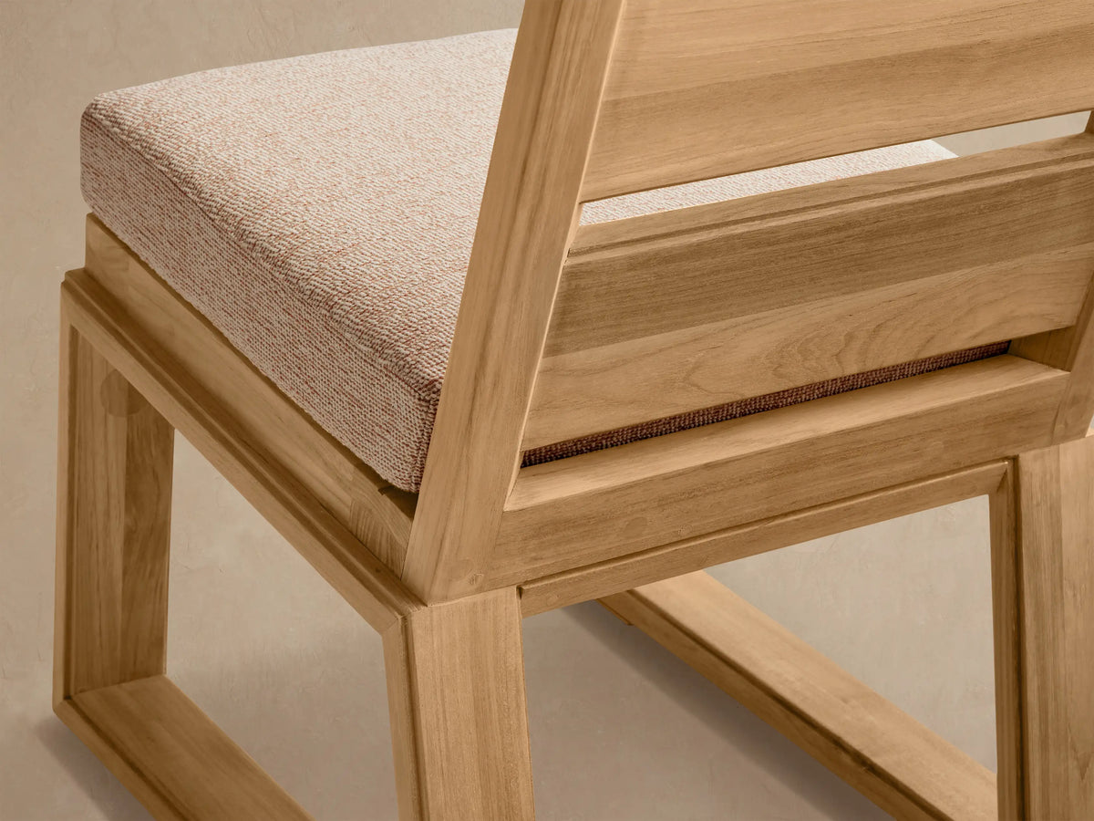 Front view of Canyon Outdoor Teak Dining Side Chair. Natural teak frame, slatted back, light beige cushion, against a textured wall.