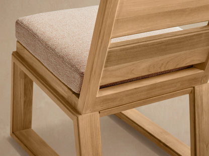Front view of Canyon Outdoor Teak Dining Side Chair. Natural teak frame, slatted back, light beige cushion, against a textured wall.