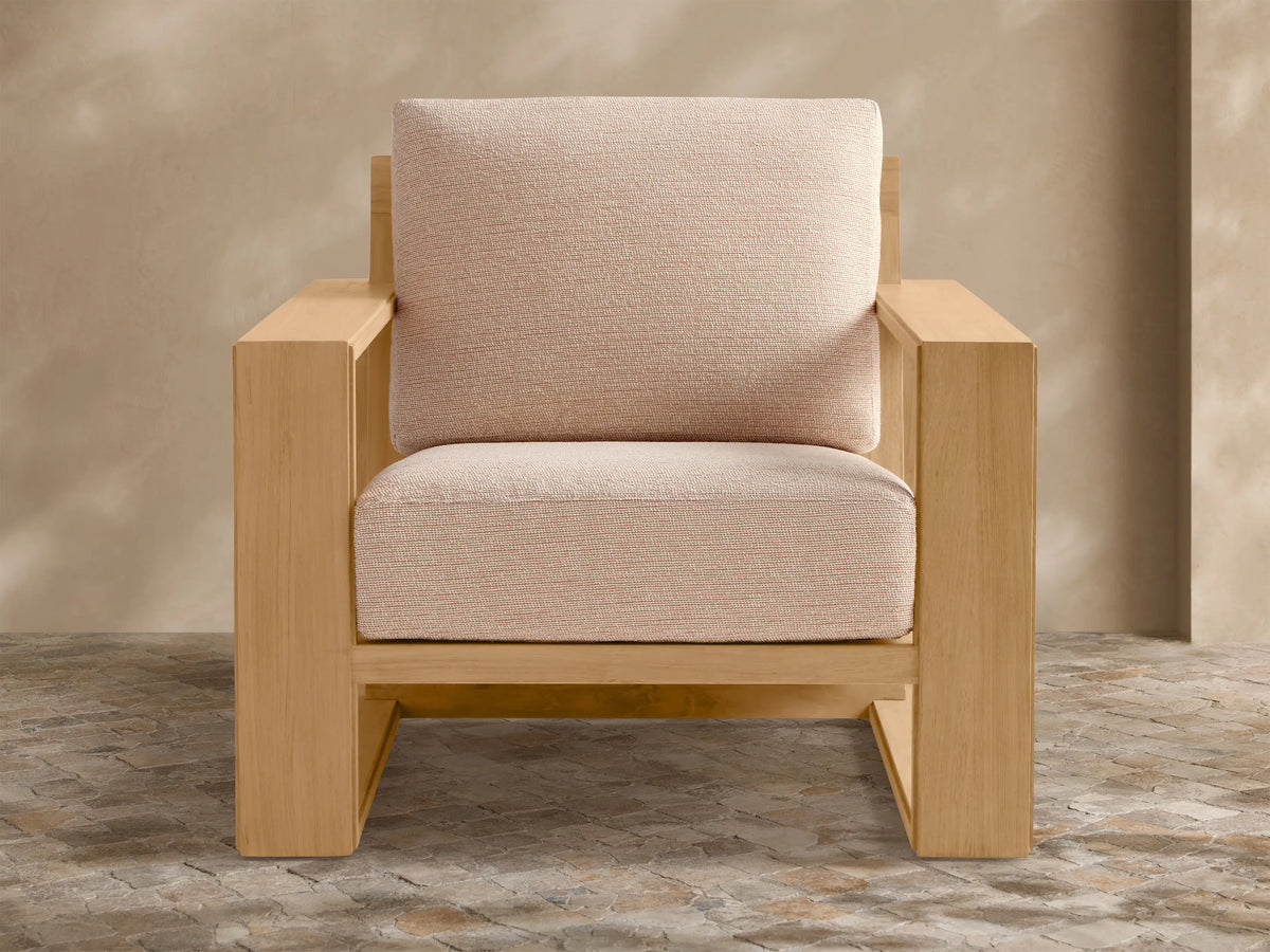 Canyon Outdoor Teak Lounge Chair. Modern teak wood frame with thick light beige fabric cushions, on a stone patio.