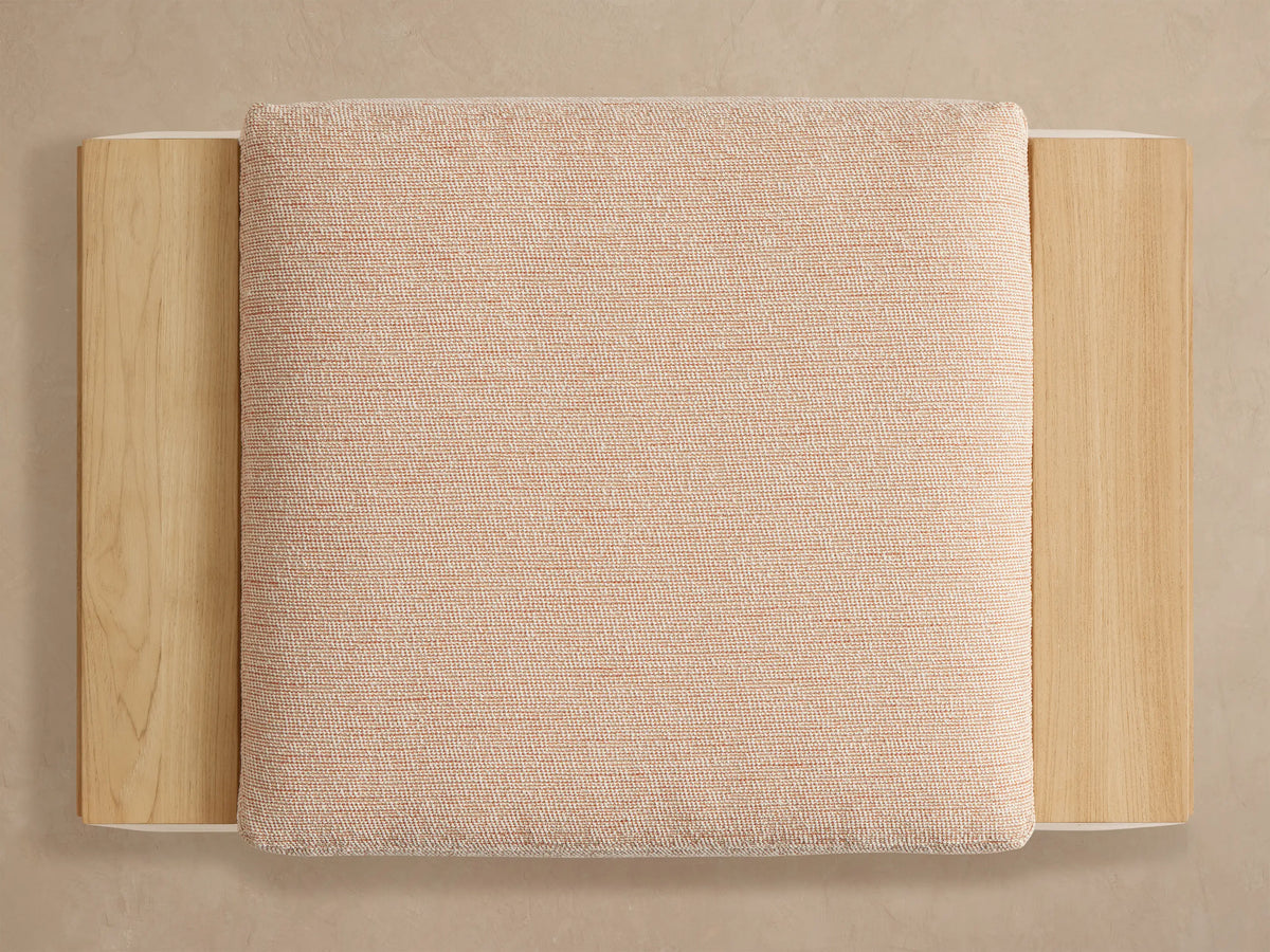 Close-up of a Canyon Outdoor Teak Ottoman. Light natural teak wood frame, woven light beige cushion with subtle orange threads.