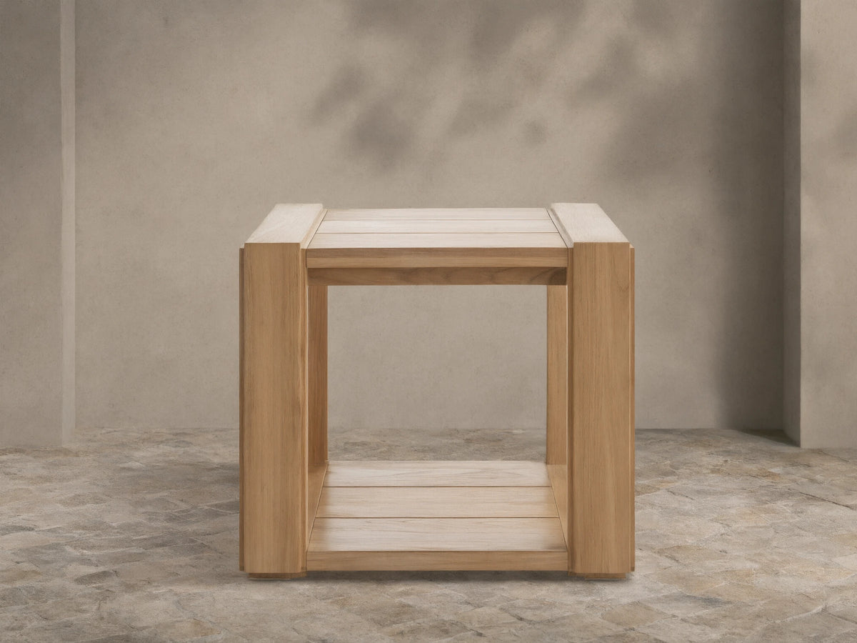 Canyon Outdoor Teak End Table, light natural teak wood, square with slatted top and bottom, on a stone patio.