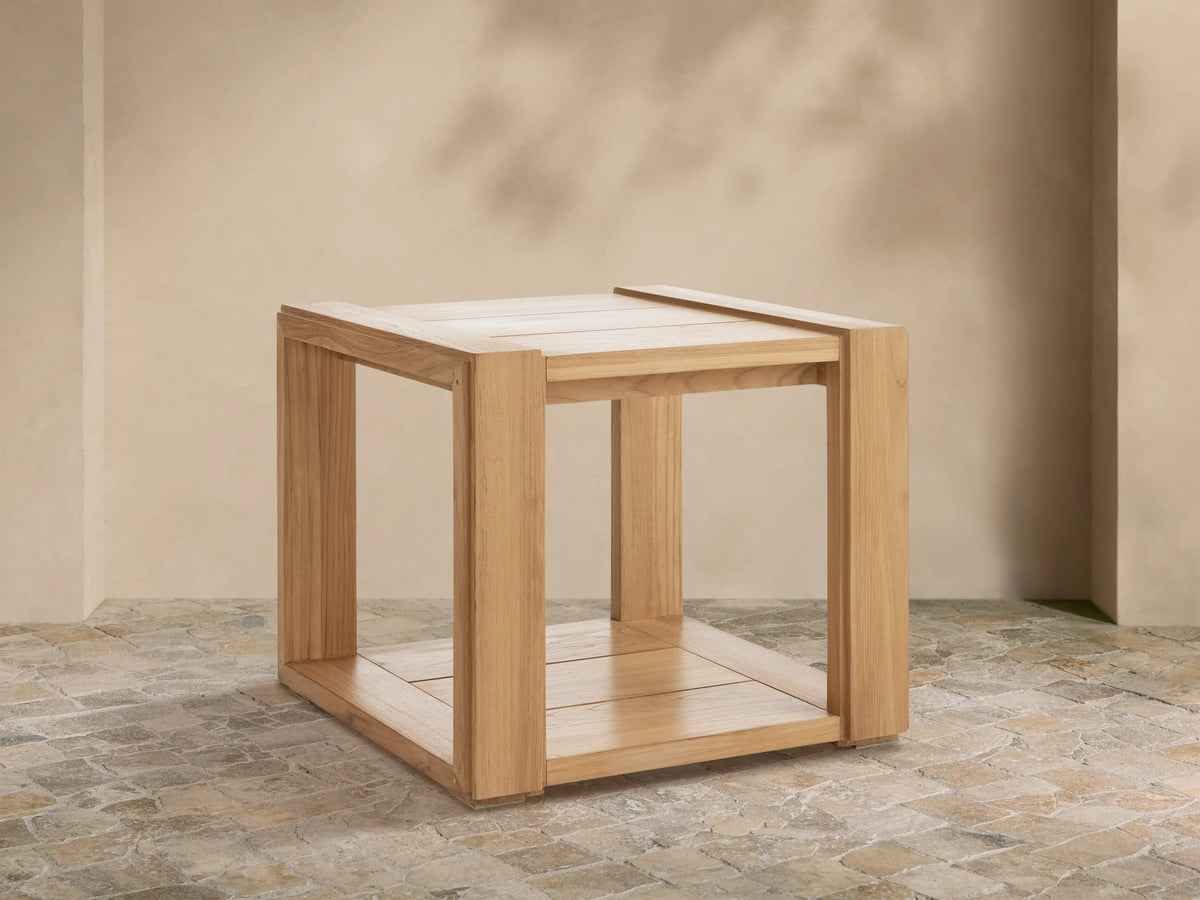 Canyon Outdoor Teak End Table, light natural teak wood, square with slatted top and bottom, on a stone patio.