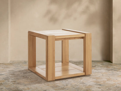 Canyon Outdoor Teak End Table, light natural teak wood, square with slatted top and bottom, on a stone patio.