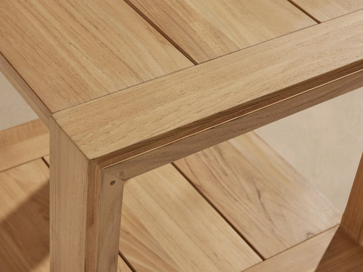 Canyon Outdoor Teak End Table, square with slatted top & bottom shelf, light natural wood, on stone patio.