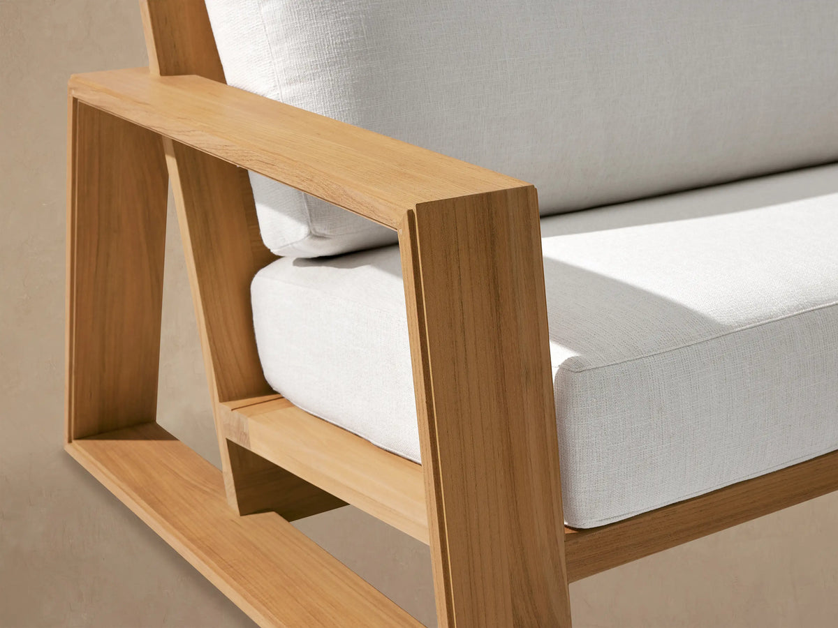 Canyon Outdoor Teak Sofa: Front view of light teak wood frame with two clean white cushions, on a light brown patio.