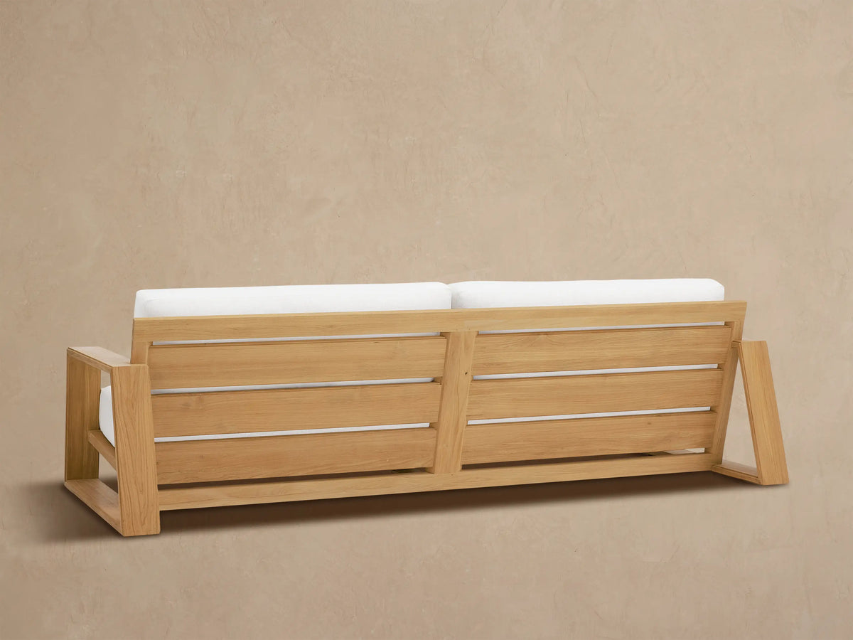 Canyon Outdoor Teak Sofa close-up: light brown teak armrest and frame, featuring light gray, textured outdoor cushions.