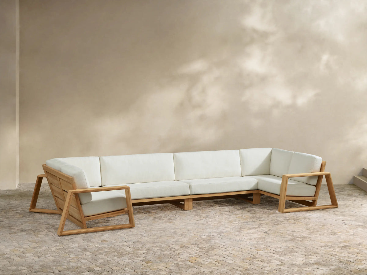Canyon Outdoor Teak 4-Piece Sectional: U-shaped light teak wood frame, thick cream cushions on a stone patio.