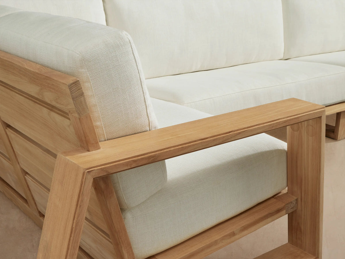 Canyon Outdoor Teak four-piece L-shaped sectional with natural wood frame & white cushions on a stone patio.