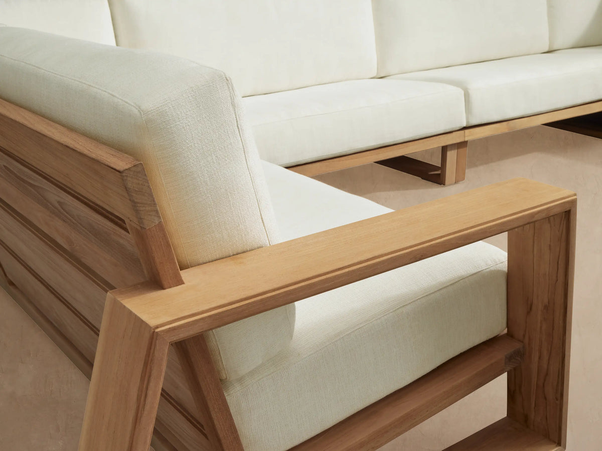 Canyon Outdoor Teak Four-Piece Sectional with natural teak wood frame and white cushions, L-shaped, on a stone patio.