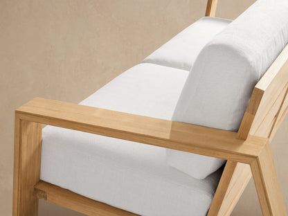Canyon Outdoor Teak Sofa, angled right, with a natural teak wood frame and plush white cushions on a paved patio.