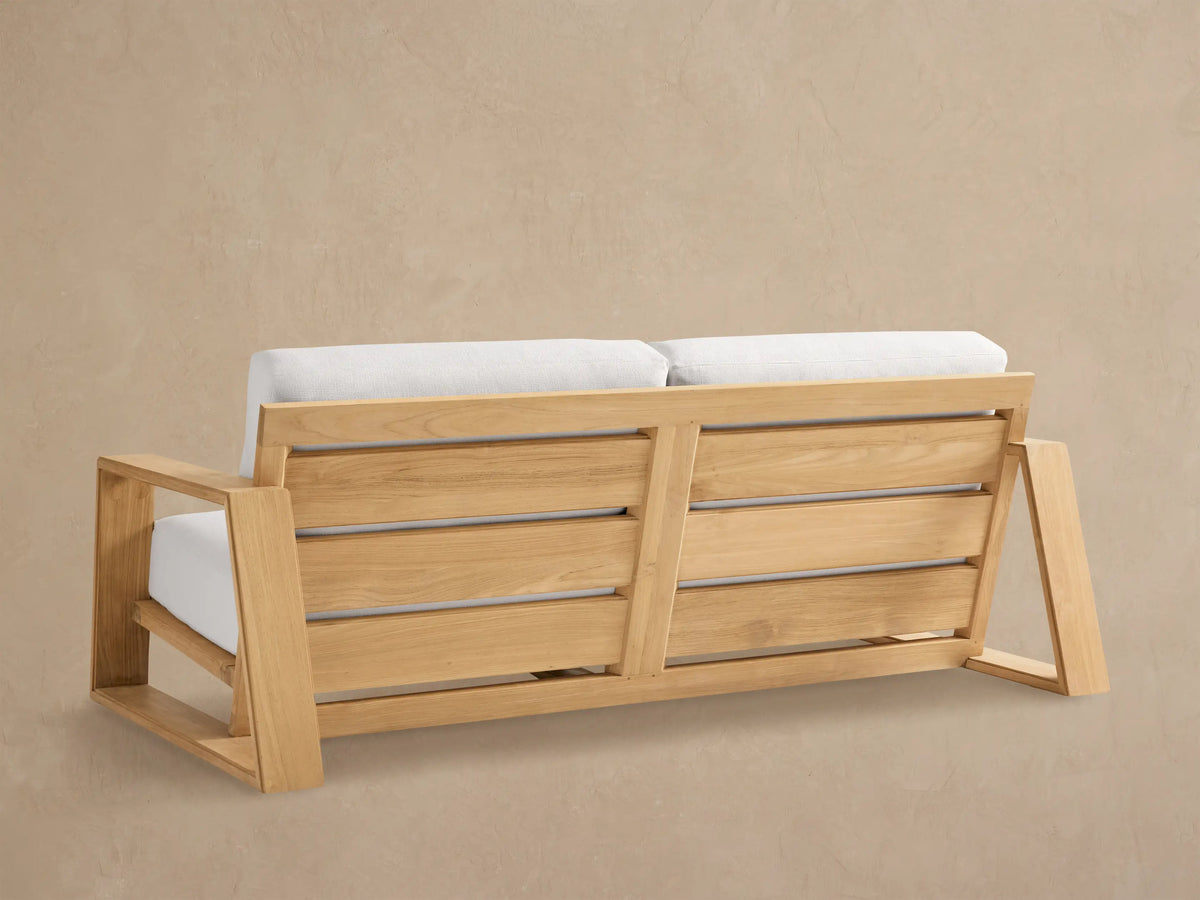 Close-up of Canyon Outdoor Teak Sofa. Light teak wood frame with thick white cushions, seen from an elevated angle.