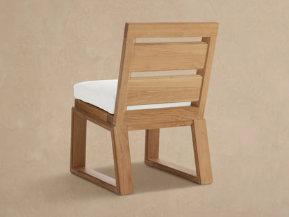 Angled close-up of Canyon Teak Dining Side Chair. Light brown teak wood frame with visible grain, part of white seat cushion.