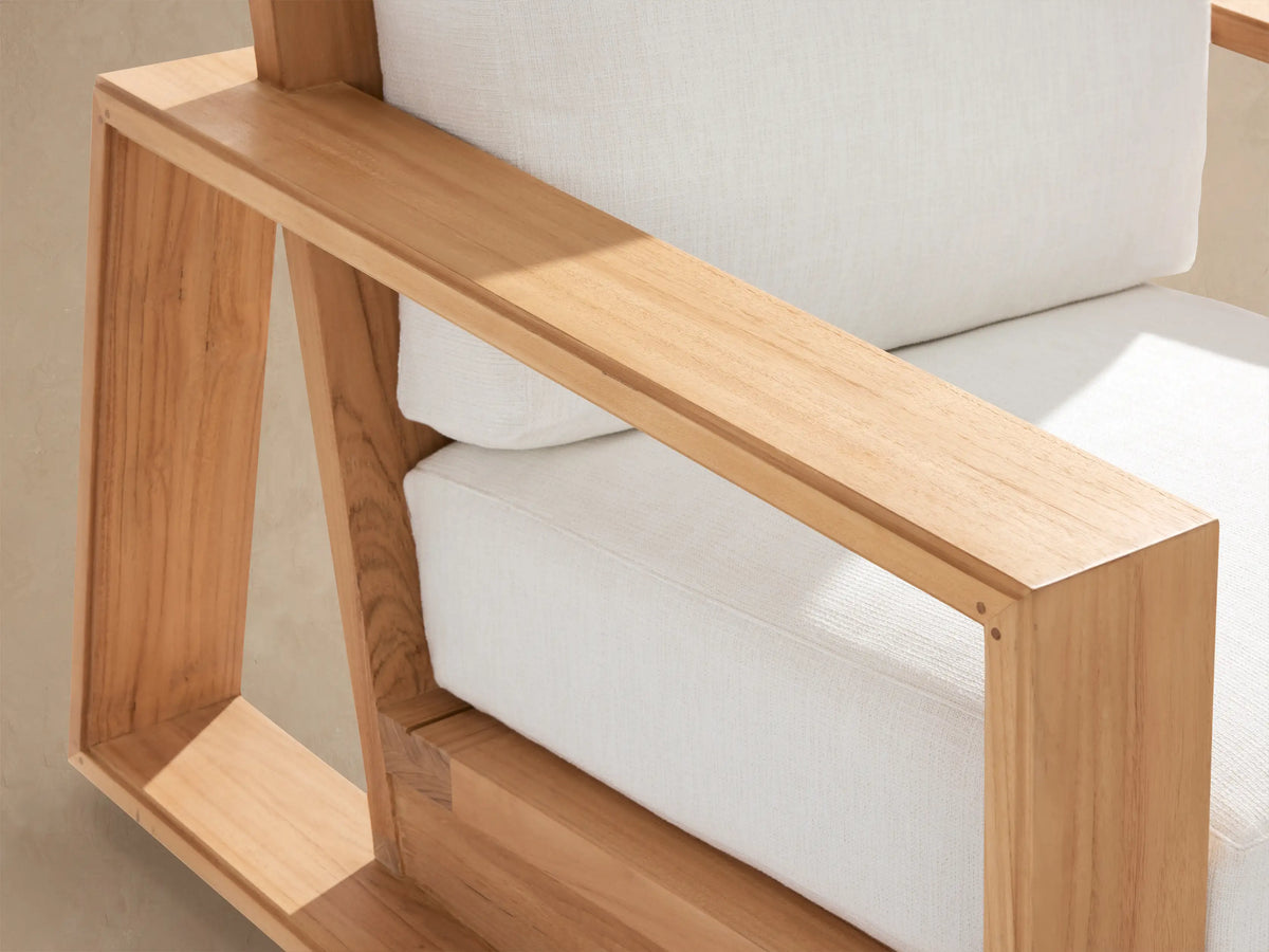 Front view of Canyon Outdoor Teak Swivel Chair with light brown teak wood frame, thick white cushions on a stone patio.