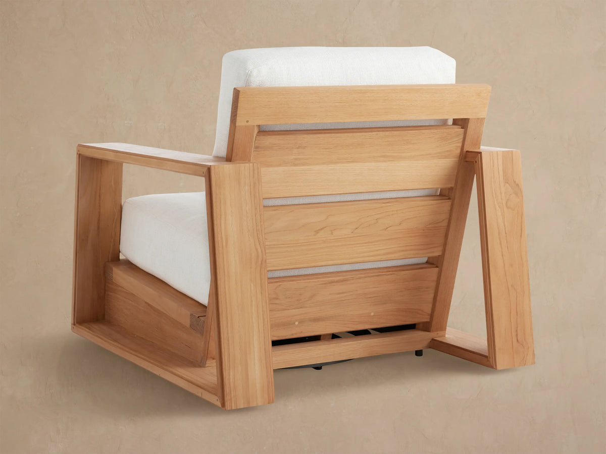 Close-up of Canyon Outdoor Teak Swivel Chair showing the smooth, angular teak armrest and bright white, textured cushions.